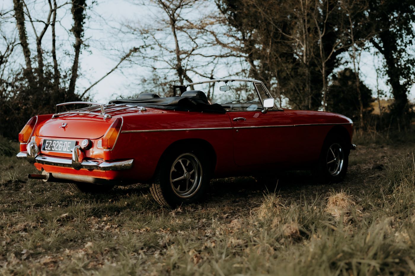 Vue latérale d'une MG B rouge, illustrant le design compact et la silhouette typique du roadster britannique.