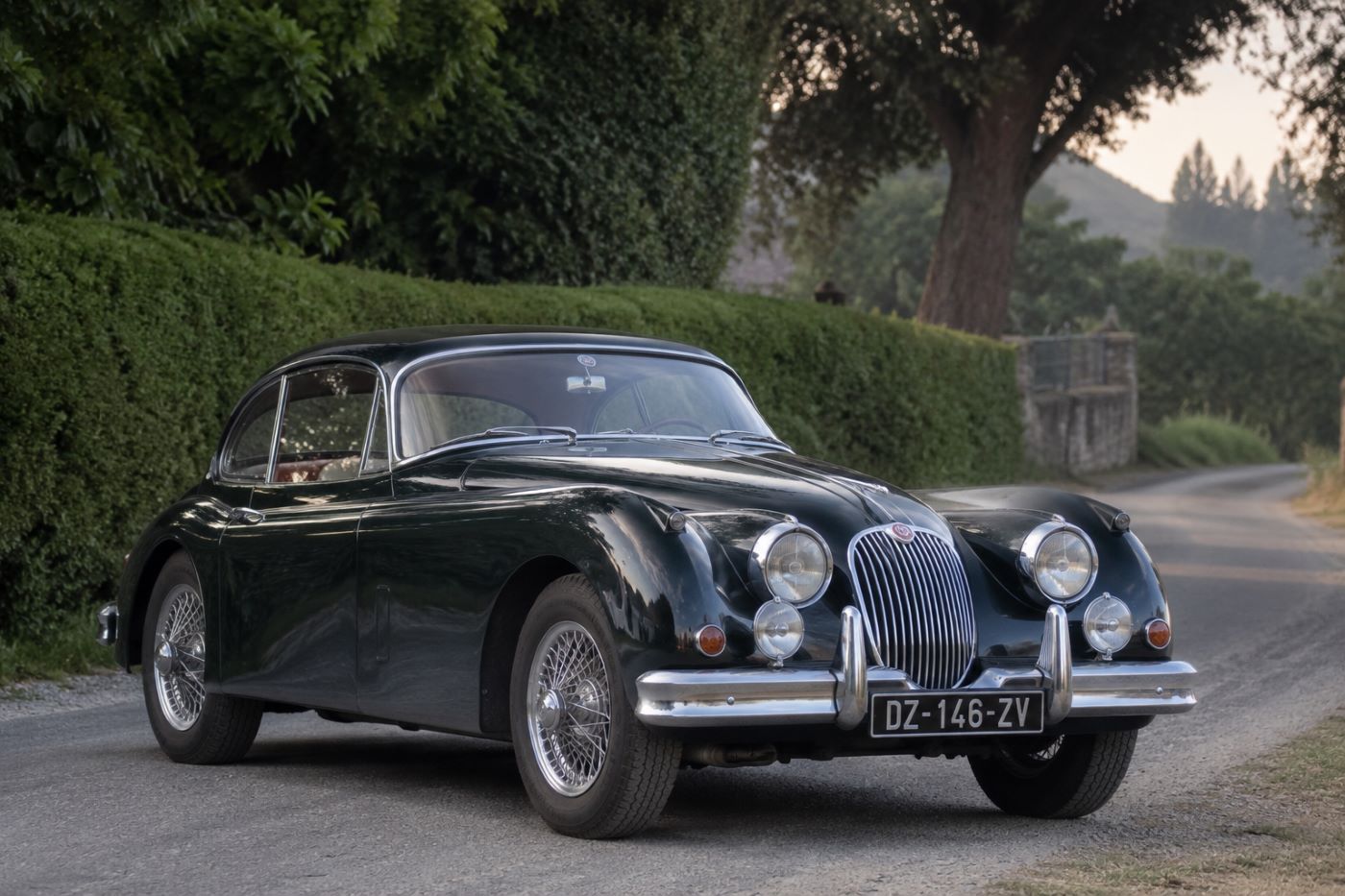 Jaguar XK150 verte vue de trois quarts avant sur une route de campagne, illustrant les lignes élégantes de la célèbre GT britannique.
