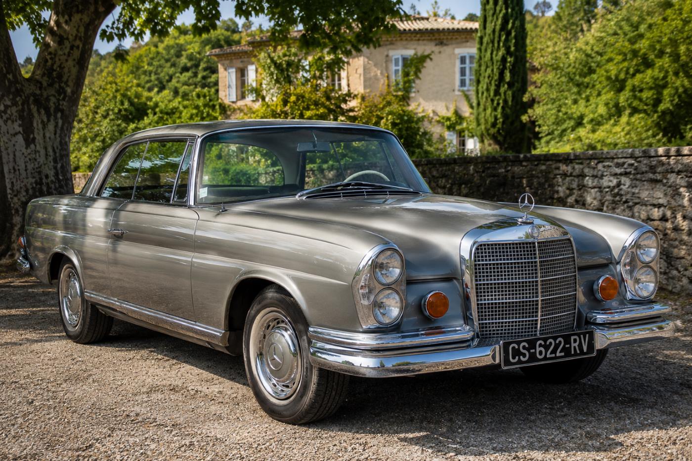 Mercedes W111 Coupé grise vue de trois-quarts avant sur une route de campagne, illustrant l'élégance intemporelle de ce coupé Mercedes de collection.