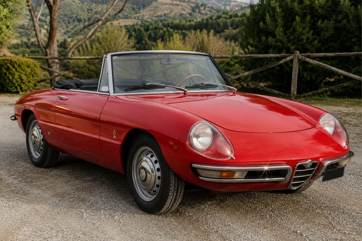 Alfa Romeo Spider Duetto rouge vue de trois quarts avant sur une route de campagne, illustrant les lignes emblématiques dessinées par Pininfarina.