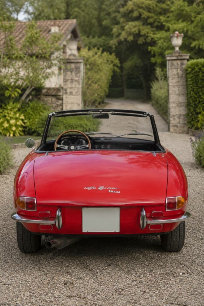 Vue arrière d'un Alfa Romeo Spider Duetto rouge avec capote repliée, illustrant les courbes caractéristiques du cabriolet italien de collection.