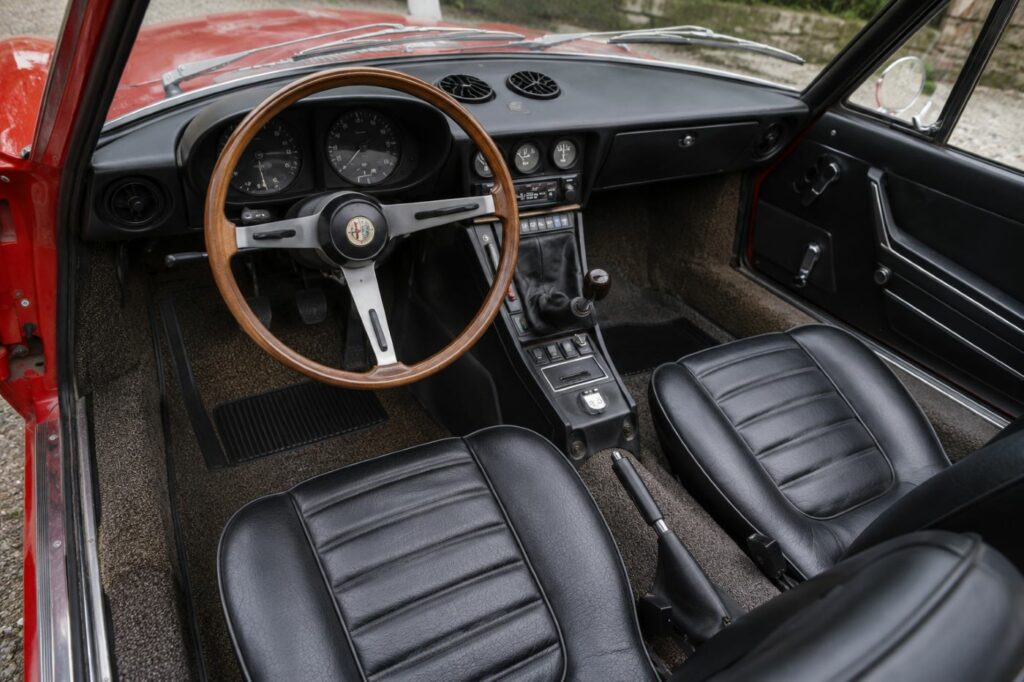 Habitacle d'un Alfa Romeo Spider Duetto avec volant en bois, instrumentation d'origine et tableau de bord typique des cabriolets italiens des années 1960.