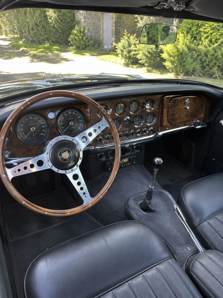 Habitacle d'une Jaguar XK150 avec tableau de bord en bois, compteurs Smiths et intérieur en cuir, typique des GT britanniques des années 1950.