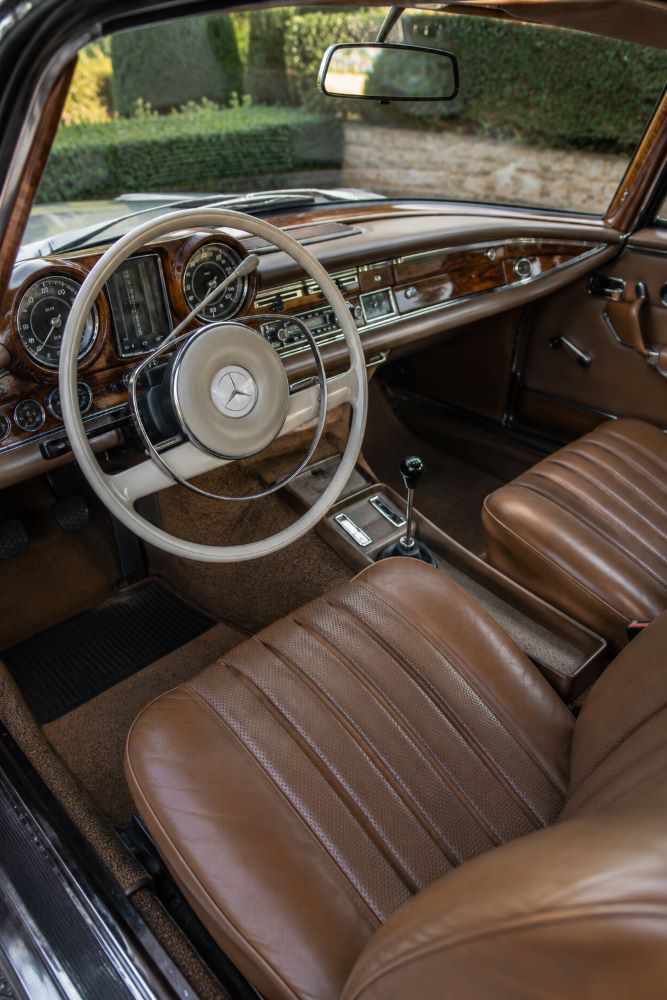Habitacle en cuir et boiseries d'une Mercedes W111 Coupé avec volant ivoire, instrumentation VDO et tableau de bord en ronce de noyer.