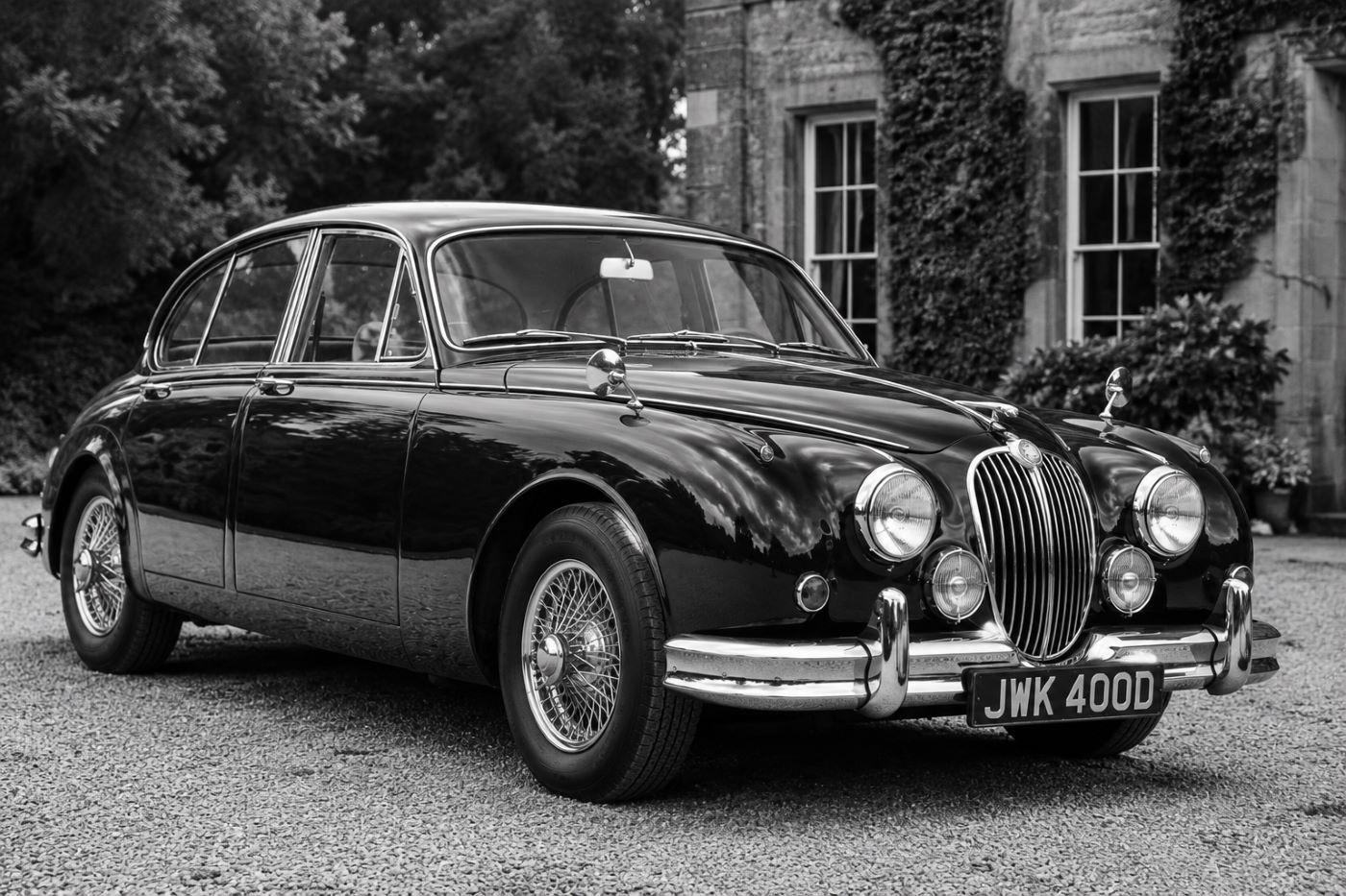 Photographie en noir et blanc d'une Jaguar MK2 des années 1960 devant une demeure britannique, illustrant l'histoire de cette berline de prestige.