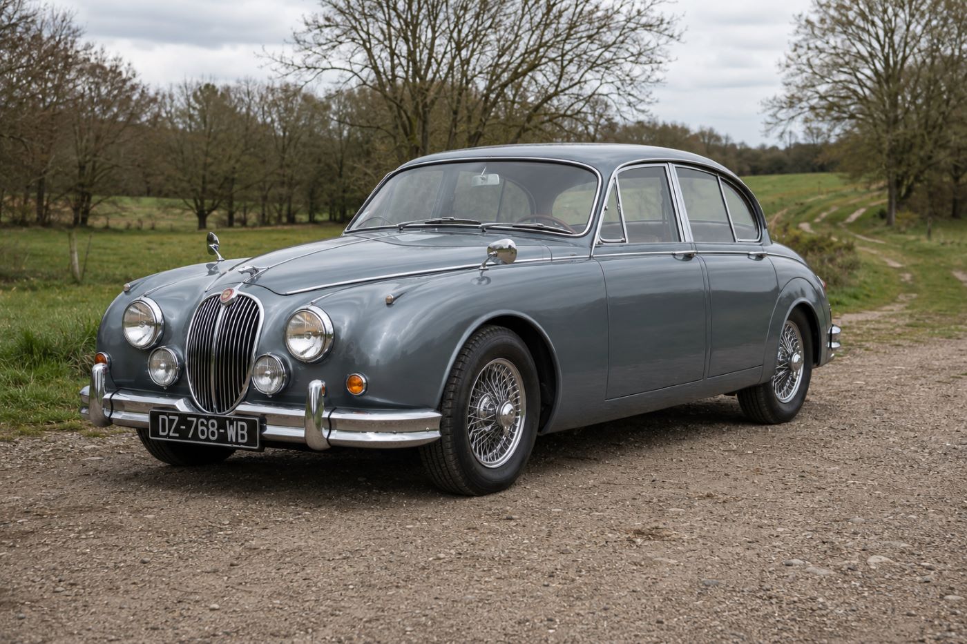 Jaguar MK2 grise vue de trois-quarts avant sur une route de campagne, illustrant l'élégance intemporelle de cette berline britannique de collection.