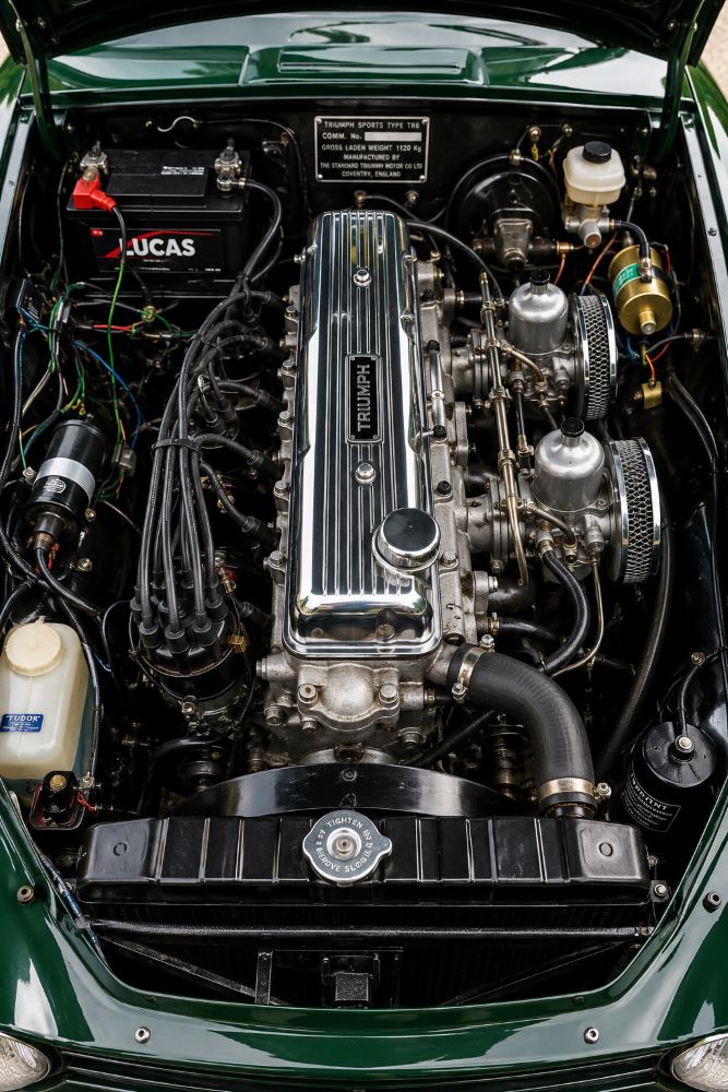 Moteur six cylindres en ligne d'une Triumph TR6 avec capot ouvert, illustrant la mécanique emblématique des roadsters Triumph.