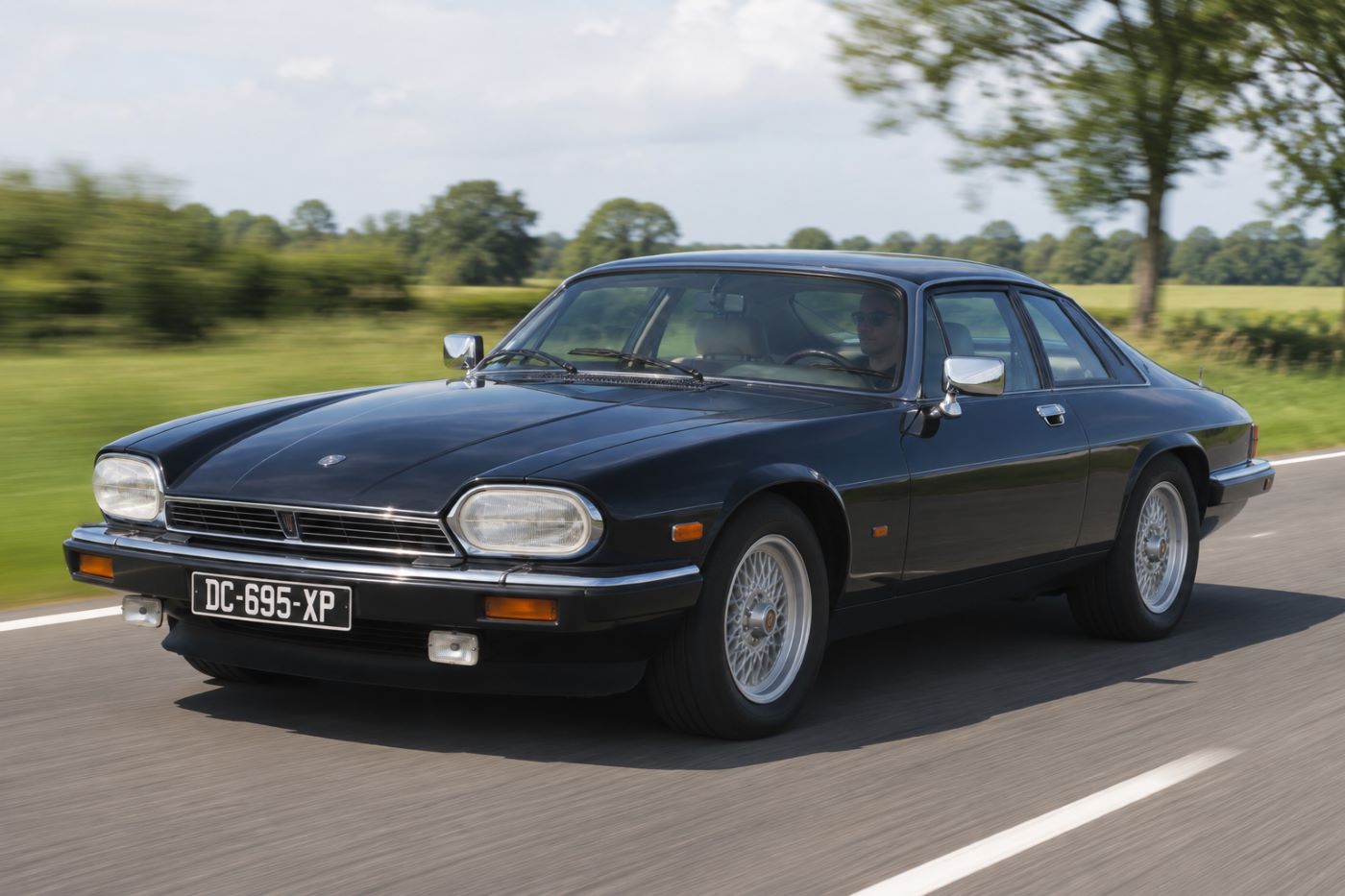 Jaguar XJS en circulation sur une route sinueuse, illustrant son confort de conduite, sa stabilité à haute vitesse et sa vocation de grande routière destinée aux longs trajets.