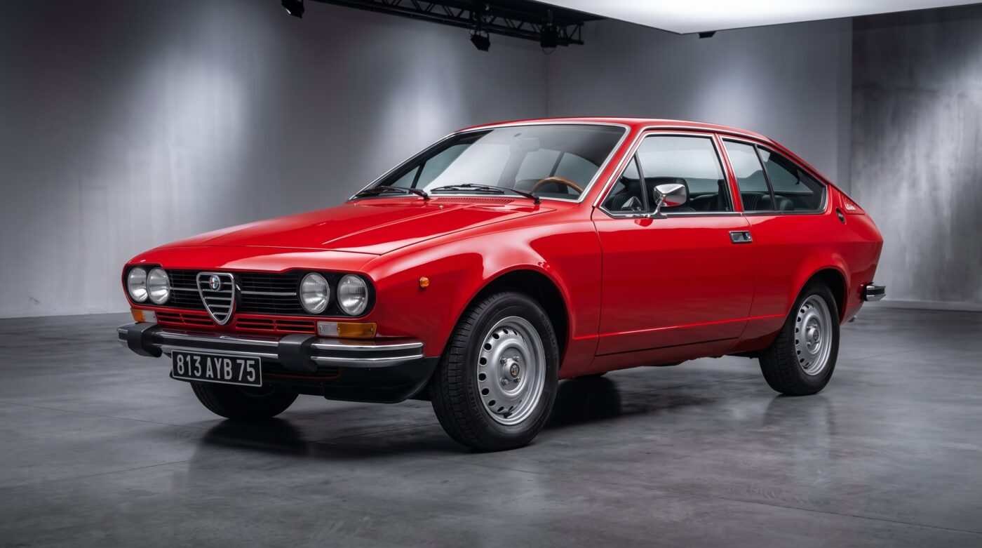 Alfa Romeo Alfetta GTV rouge vue de trois quarts avant sur fond neutre, carrosserie d'origine impeccable.