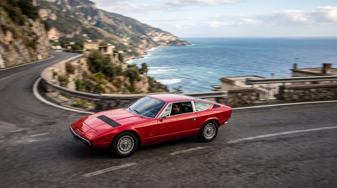 Maserati Khamsin 1974 rouge en plein essai routier sur une route sinueuse, illustrant ses performances et son élégance.