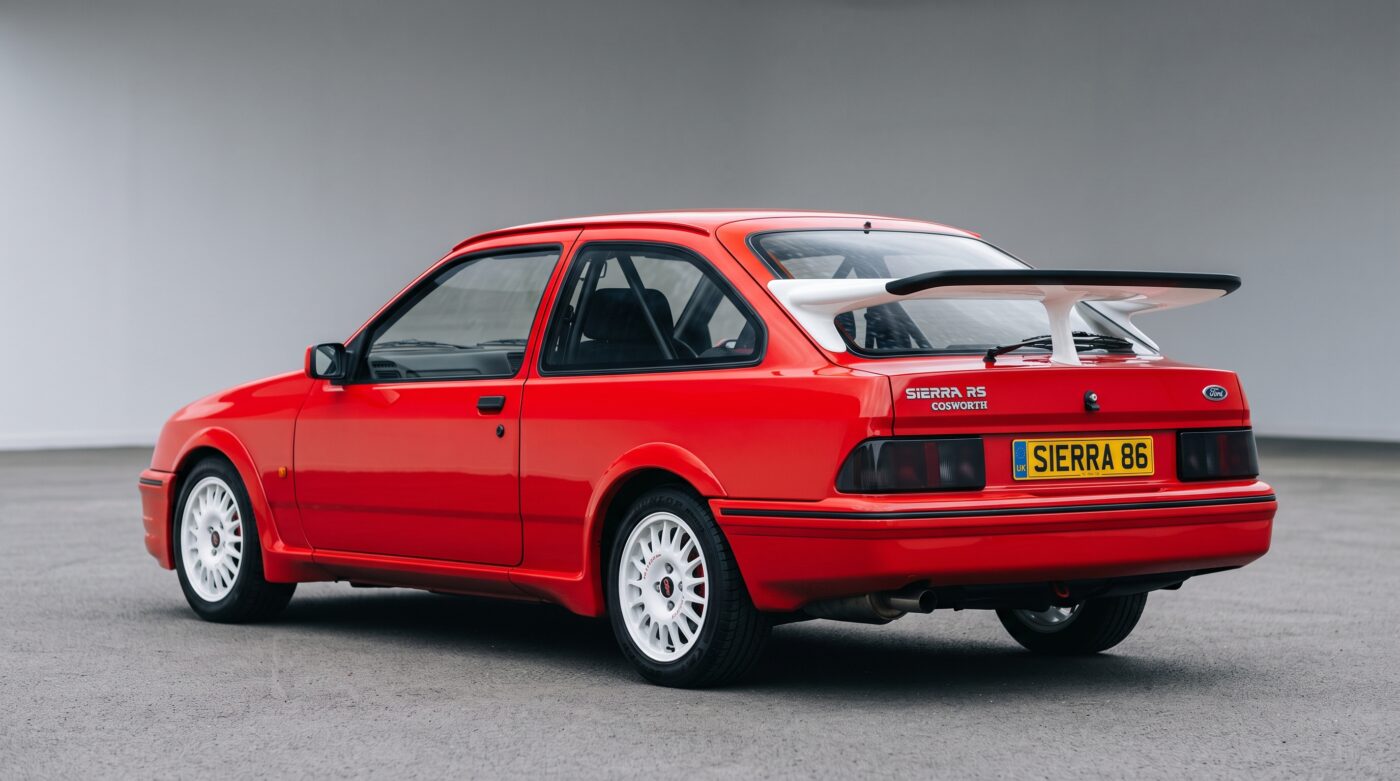 Ford Sierra RS Cosworth rouge vue de trois quarts arrière avec son aileron biplan caractéristique et ses feux arrière d'origine.