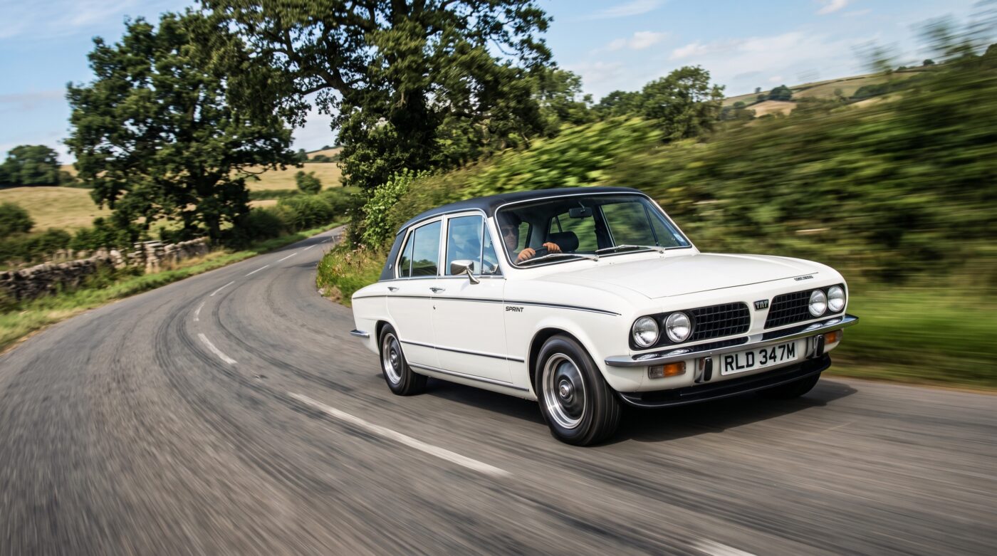 Triumph Dolomite Sprint blanche en plein essai routier sur une route sinueuse, capturant le plaisir de conduite.